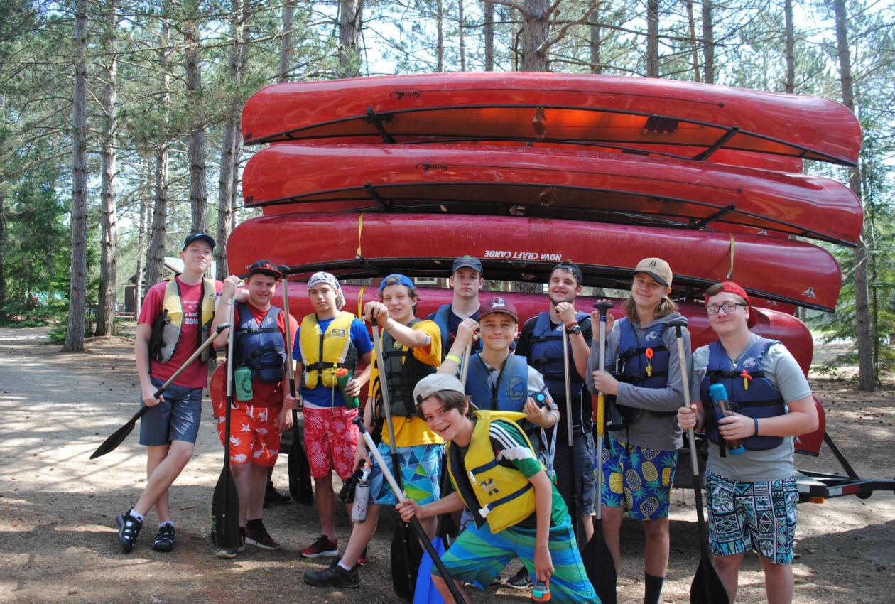 Male cabin group pictured in front of canoe trailer with paddles in hand.